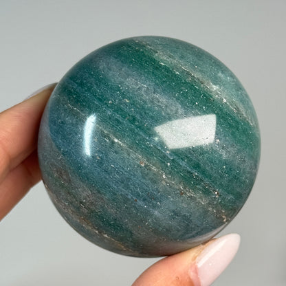 Teal Aventurine Sphere #2, held in hand, showing teal-green coloring with brown patches.