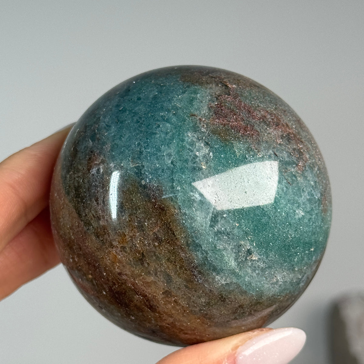 Teal Aventurine Sphere #6, held in hand, showing teal-green and brown mottled patterns.