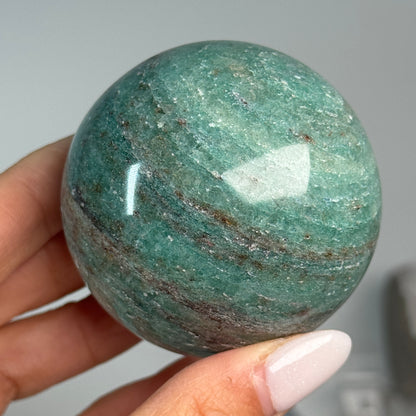 Teal Aventurine Sphere #7, held in hand, showing green coloring with fine mottled patterns.