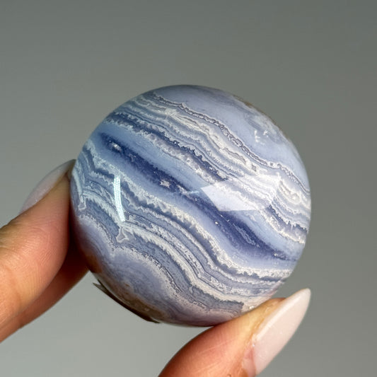 Blue Lace Agate Sphere #1, held in hand, showing blue and white wavy bands.