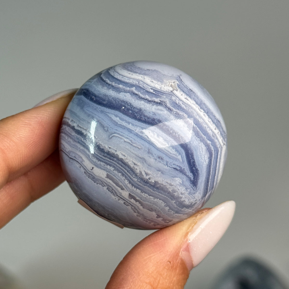 Blue Lace Agate Sphere #12, held in hand, showing blue and white banding with a brown mineral seam.