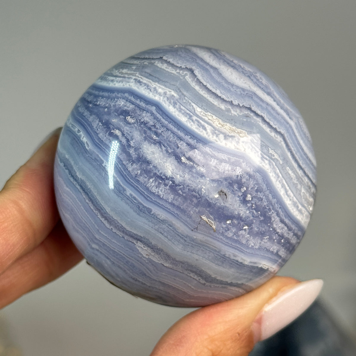 Blue Lace Agate Sphere #4, held in hand, showing fine blue and white layered bands.