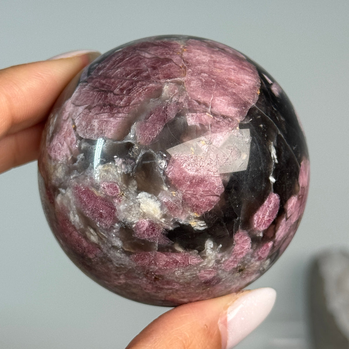 Rubellite (Pink Tourmaline) with Smoky Quartz Sphere #12, held in hand, showing pink, black and cream mineral patterns.