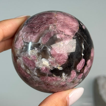 Rubellite (Pink Tourmaline) with Smoky Quartz Sphere #12, held in hand, showing pink, black and cream mineral patterns.