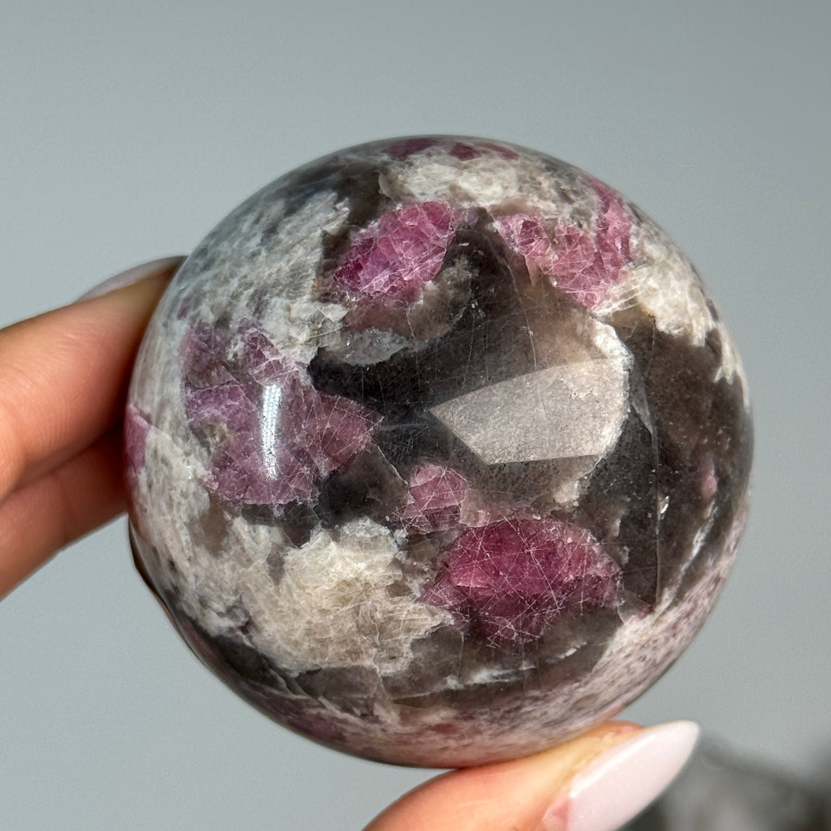 Rubellite (Pink Tourmaline) with Smoky Quartz Sphere #5, held in hand, showing pink, black and cream mineral patterns.
