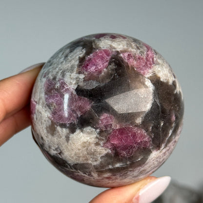 Rubellite (Pink Tourmaline) with Smoky Quartz Sphere #5, held in hand, showing pink, black and cream mineral patterns.