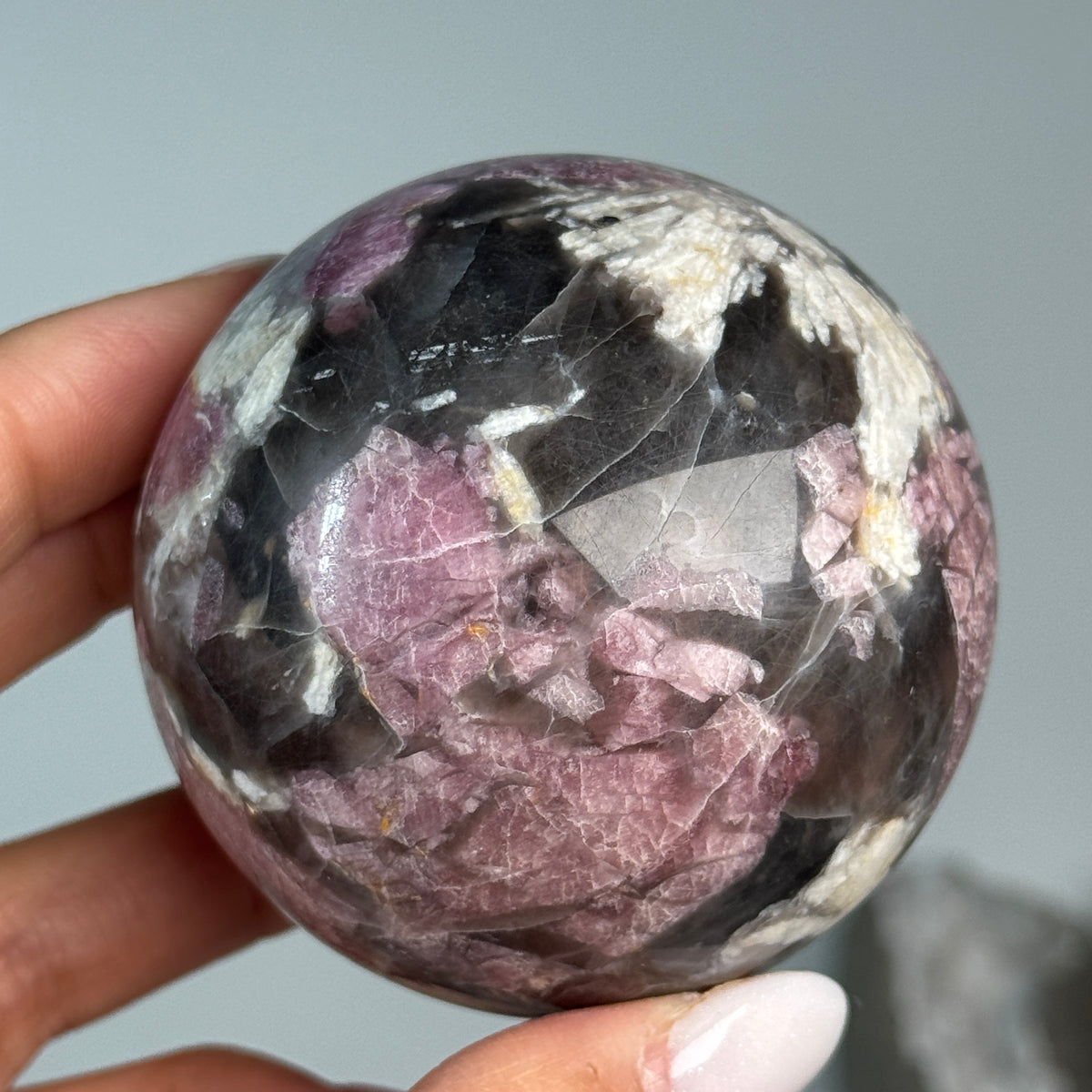 Rubellite (Pink Tourmaline) with Smoky Quartz Sphere #9, held in hand, showing pink, black and cream mineral patterns.