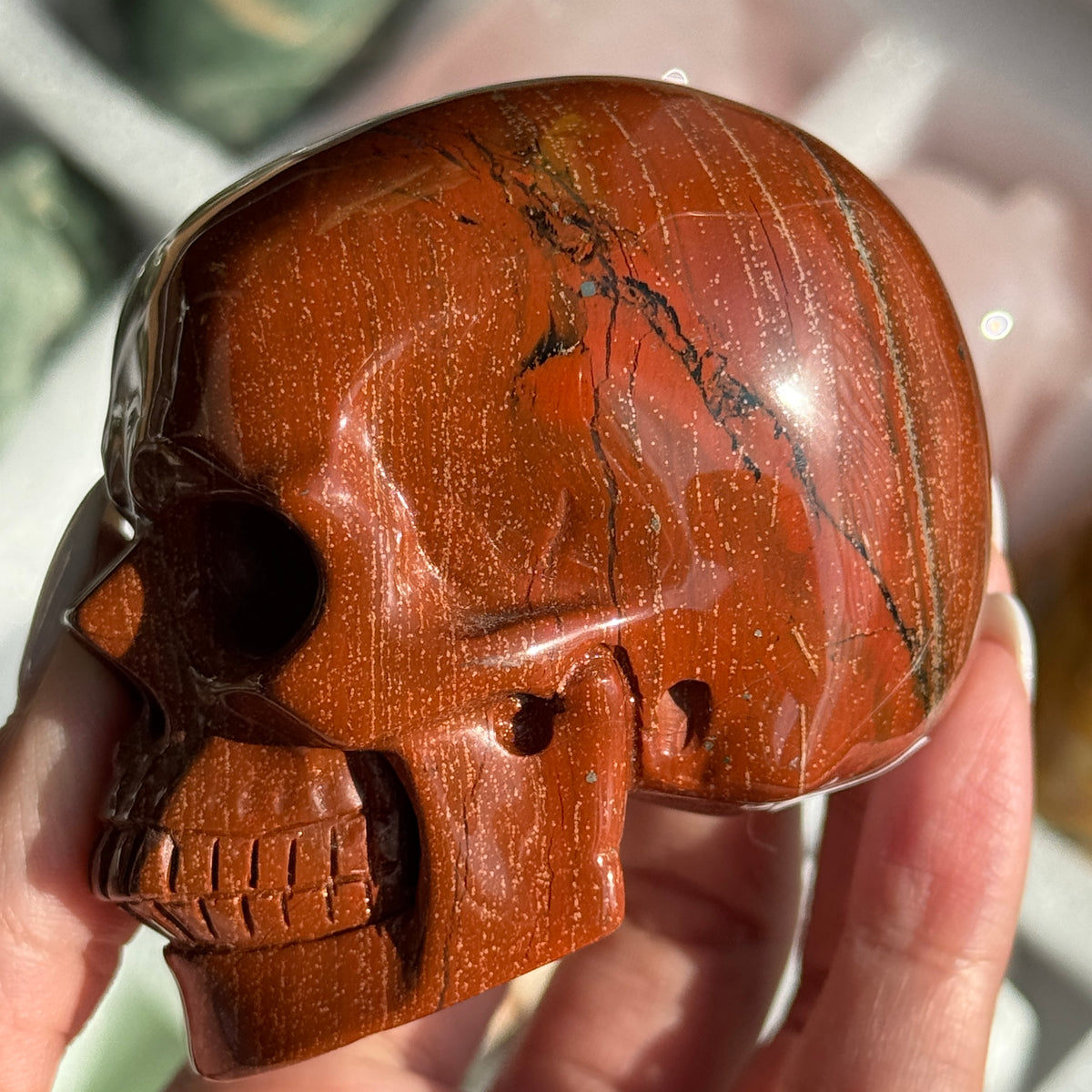 Skull Carving - Red Jasper #14, opposite side view showing rust-red coloring with fine dark veins.