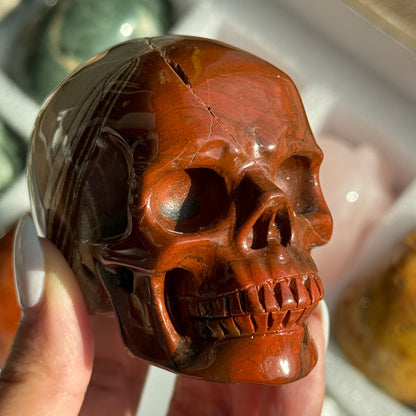 Skull Carving - Red Jasper #15, front view showing rust-red coloring with cream and gray banding.