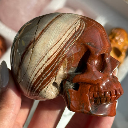 Skull Carving - Red Jasper #15, side view showing rust-red coloring with cream and gray banding.