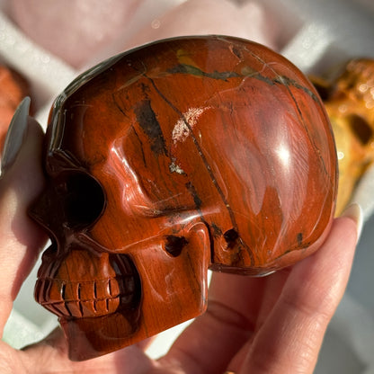 Skull Carving - Red Jasper #15, opposite side view showing rust-red coloring with cream and gray banding.